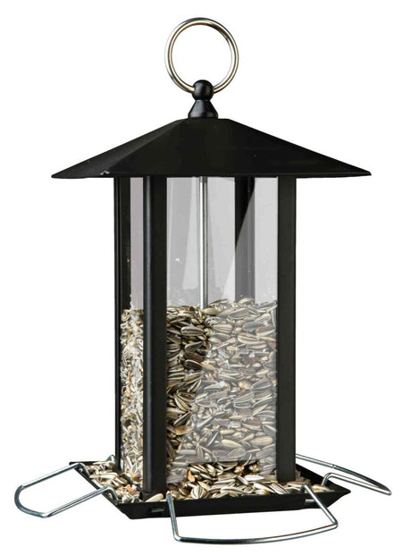 Schwarzes sechseckiges Vogelhaus mit klarem Kunststoffkörper, gefüllt mit Sonnenblumenkernen, und Metallbügel am Dach.