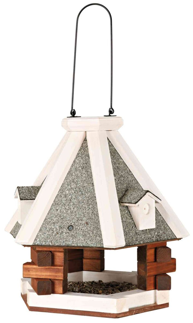 Sechseckiges Vogelhaus mit grauem Dach, hölzernem Rahmen und Aufhängebügel, gefüllt mit Sonnenblumenkernen.