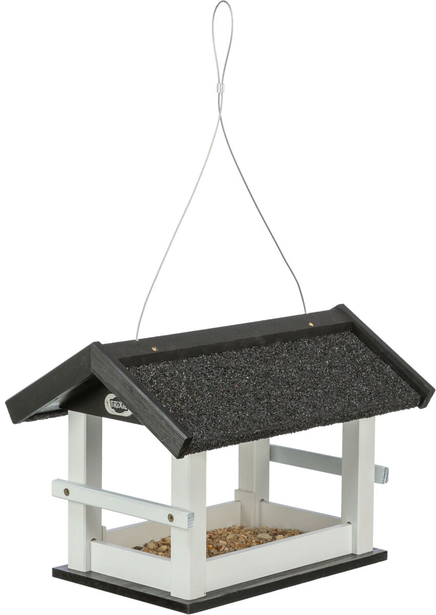 Ein schwarzes und weißes hölzernes Vogelhaus mit Kieseln, hängend an einem Metallseil.