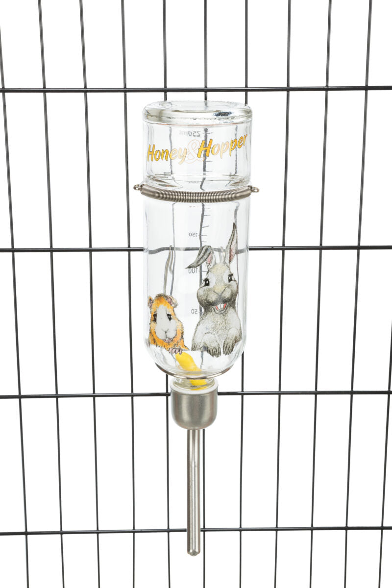 Transparente Wasserflasche mit tierischen Illustrationen und Schriftzug "Honey &amp; Hopper" an einem Gitter befestigt.