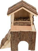 Kleines Holzhaus mit Rinde, vorne offen und mit Naturmaterialien gefüllt, über einer kleinen Plattform.