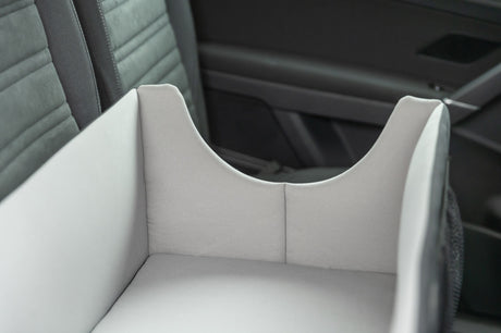 Hellgraue Transportbox auf dem Rücksitz eines Autos aus grauem Stoff.