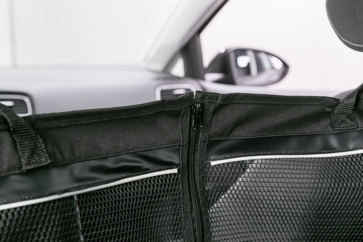 Schwarzes Trennnetz mit Reißverschluss in einem Auto, Hintergrund zeigt verschwommene Autoinnenteile.