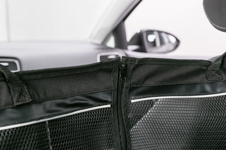 Schwarzes Trennnetz mit Reißverschluss in einem Auto, Hintergrund zeigt verschwommene Autoinnenteile.