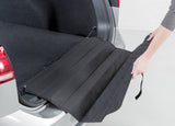 Offener Kofferraum eines Autos mit schwarzem Kofferraumteppich, der von einer Hand ausgerollt wird.