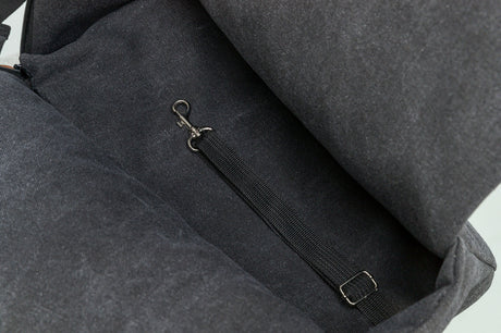 Innenbereich einer dunkelgrauen Tasche mit einem Nylongurt, der an einem kleinen Metallhaken befestigt ist.
