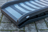 Eine schwarze Rampe mit grauen Streifen liegt auf einem gepflasterten Untergrund.