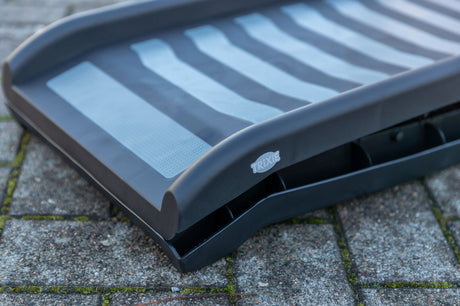 Eine schwarze Rampe mit grauen Streifen liegt auf einem gepflasterten Untergrund.