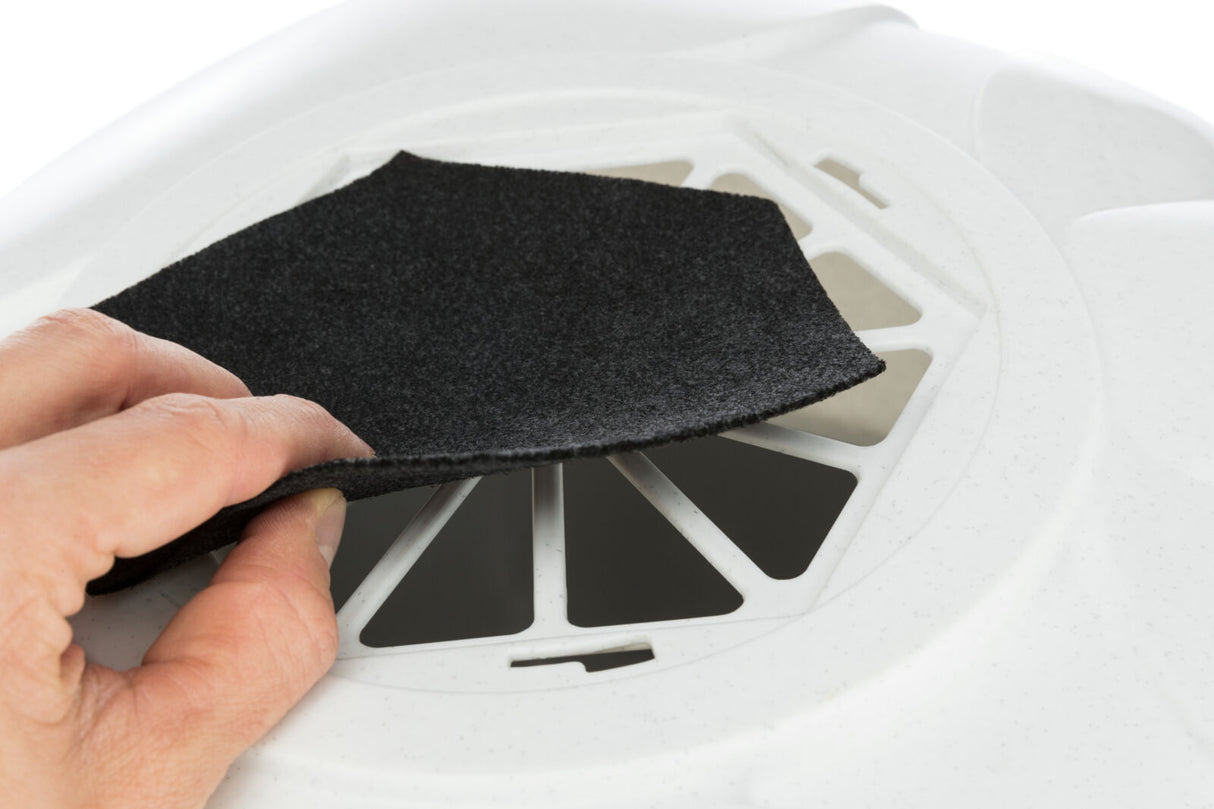 Eine Hand hält ein schwarzes, rechteckiges Stück Stoff vor einer weißen, ventilartigen Abdeckung.