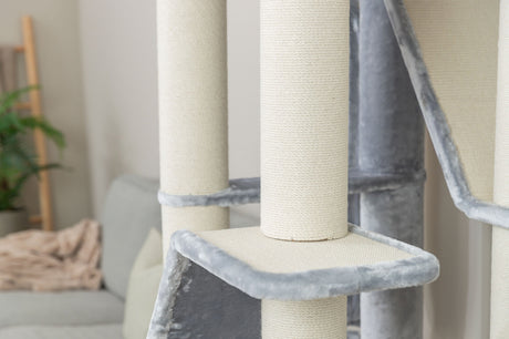 Kratzturm aus hellem Stoff mit grauen Plüscheinfassungen vor Sofa im Wohnzimmer.