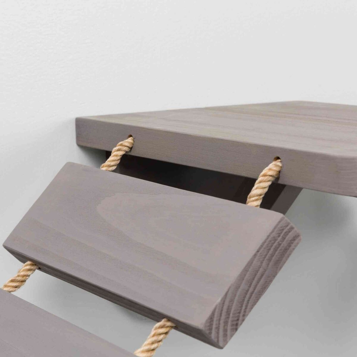 Graue Holzstufen, die mit einer dicken, hellen Seilkordel an einer weißen Wand befestigt sind.