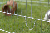Metallgitter mit Kette und Karabiner vor verschwommenem grasbewachsenem Hintergrund.