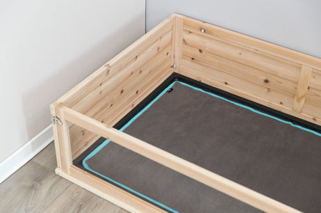Holzumrandung umgibt eine rechteckige, graue Matte mit türkisfarbenem Rand auf einem Holzfußboden neben einer weißen Wand.