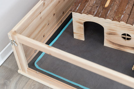Holzgehäuse mit Streuunterlage und kleinem Haus, braun und blau, auf einem Holzboden.