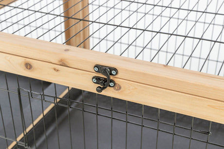 Holzrahmen mit schwarzem Drahtgitter und Metallhaken-Verschluss auf schwarzem Boden.