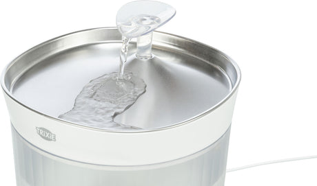 Ein weißer Trinkbrunnen mit fließendem Wasser über einer metallisch glänzenden Oberfläche.