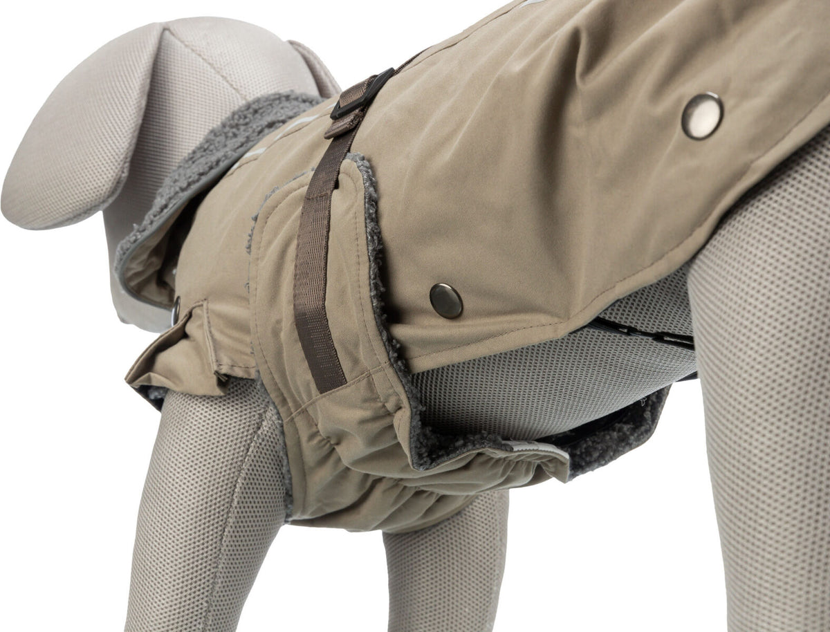 Grauer Hundemantel mit Fellfutter und Druckknöpfen auf einem textilen Hundemodell in Beige und Grau.