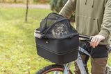 Kleiner Hund sitzt in einem schwarzen Fahrradkorb mit Netzabdeckung.