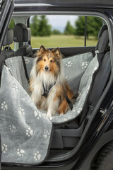 Hund sitzt in grauer Autodecke mit Pfotenmuster im Auto.