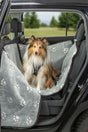 Hund sitzt in grauer Autodecke mit Pfotenmuster im Auto.
