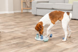 Kleiner Hund spielt mit Intelligenzspielzeug auf einem Holzfußboden in einem Wohnzimmer.