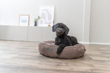 Schwarzer Hund liegt auf braunem Hundebett auf hellem Holzboden in modernem Raum.