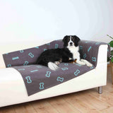 Ein Hund liegt auf einem weißen Sofa, bedeckt mit einer grauen Decke mit blauen Knochenmotiven.