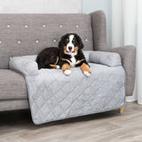 Ein Hund liegt auf einem grauen, gepolsterten Sofa mit gesteppter Decke.