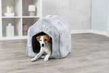 Hund sitzt in einer grauen, mit Pfotenmuster versehenen Höhle auf Holzboden.