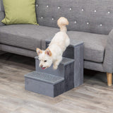 Ein weißer Hund springt von grauen Stufen, die vor einem grauen Sofa mit grünem Kissen stehen.