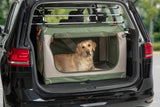 Ein Hund liegt in einem grünen Transportkäfig im Kofferraum eines Autos.