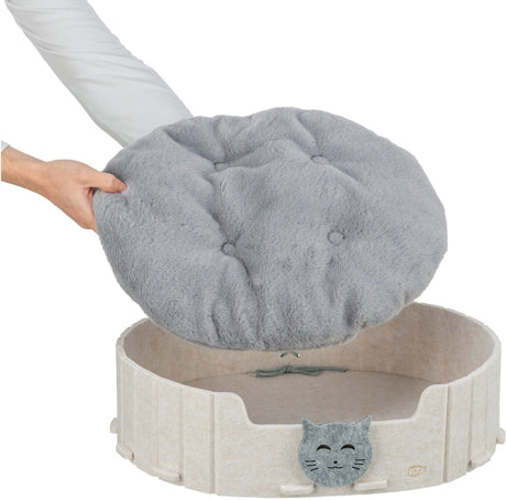 Person hebt ein graues Kissen aus einem beige-farbenen Katzenbett mit Katzenmotiv.