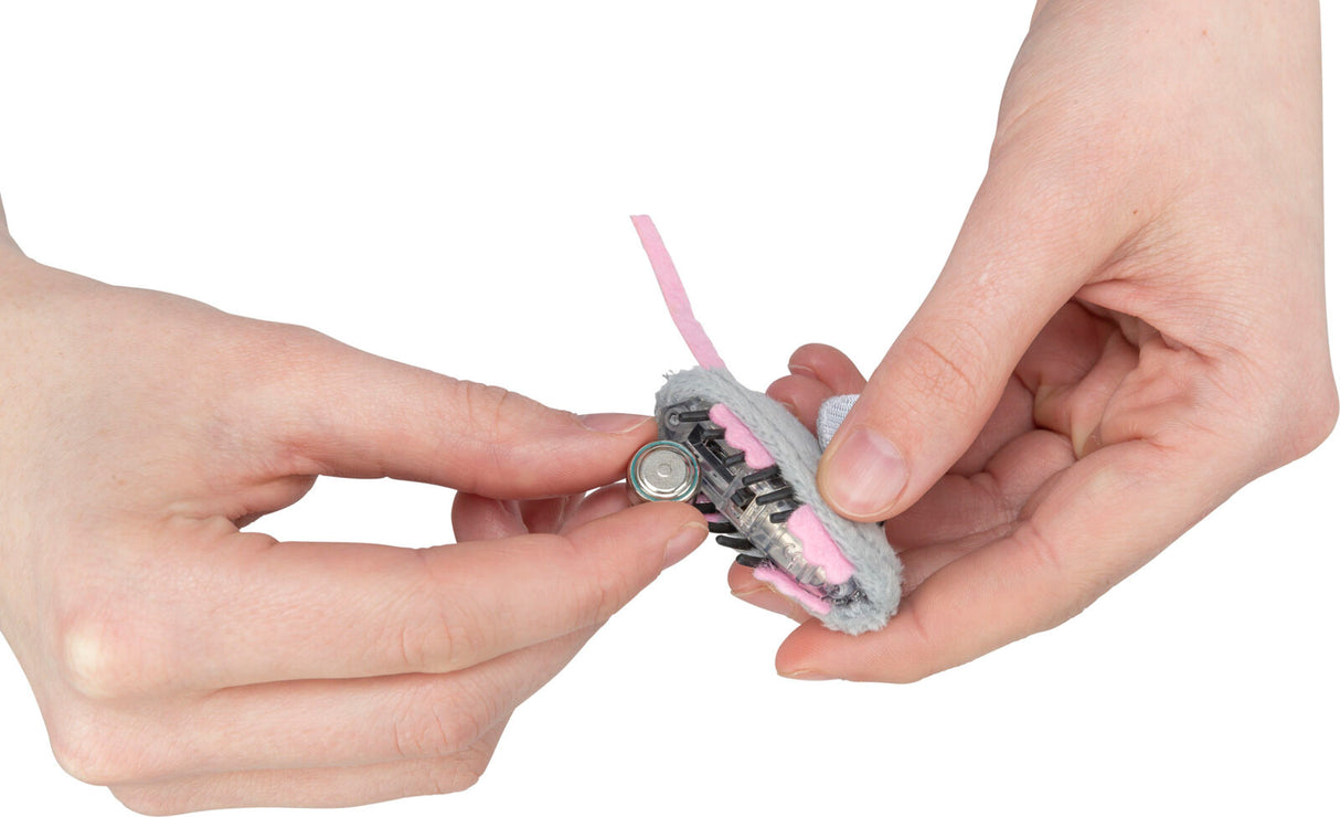 Hände halten ein graues, plüschiges Objekt mit einer pinken Komponente, eine kleine Batterie wird eingesetzt.