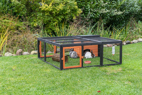 Kleintiergehege aus Metall mit Holzdetails auf grünem Rasen, innen zwei Kaninchen und Spielzeug.