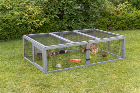 Freigehege aus Metallgitter steht auf einer Wiese, mit Kleintierunterkunft und Spielzeug.