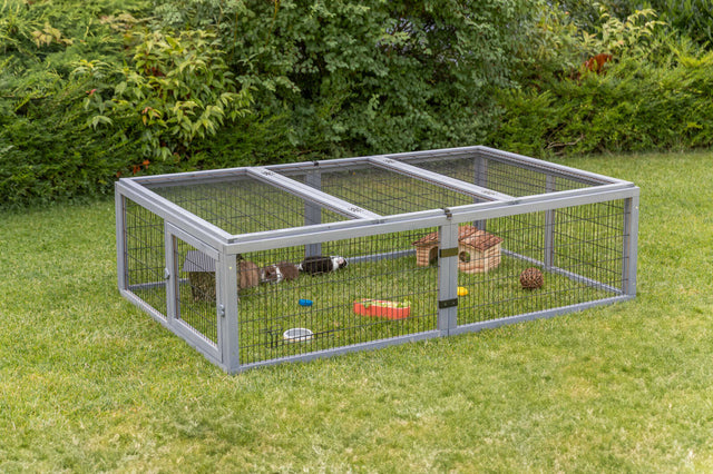 Freigehege aus Metallgitter steht auf einer Wiese, mit Kleintierunterkunft und Spielzeug.