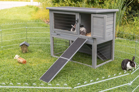 Graues Kaninchengehege mit Rampe und zwei Kaninchen auf grünem Rasen im Freien.