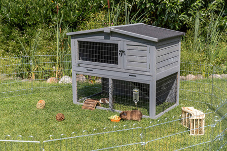 Graues Kaninchenhäuschen auf grüner Wiese mit Kaninchen und Futter im Auslaufgehege.