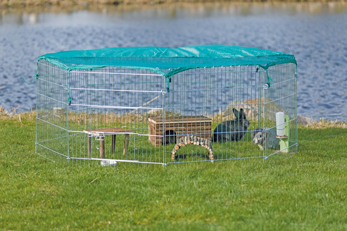 Metallgehege mit grünem Dach auf einer Wiese, innen zwei Kaninchen neben Holzhäuschen und Trinkflasche.