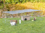 Metallkäfig auf grünem Rasen enthält zwei Kaninchen, ein kleines Haus, eine Wasserflasche und einen Futternapf.