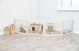 Holzgehege mit Kaninchen, Haus und Heuraufe auf hellem Holzboden, daneben drei Laternen mit Kerzen.