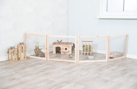 Holzgehege mit Kaninchen, Haus und Heuraufe auf hellem Holzboden, daneben drei Laternen mit Kerzen.