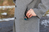 Eine Person in einem grauen Mantel steckt die Hand in eine Tasche, die etwas enthält, Hintergrund unscharf.