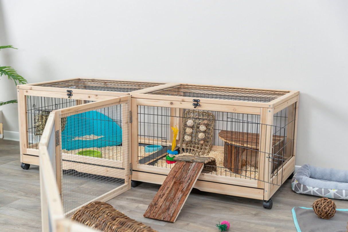 Holzkäfig mit Drahtgitter und Rampen, ausgestattet mit Spielsachen und Liegeflächen, steht auf einem Holzboden.