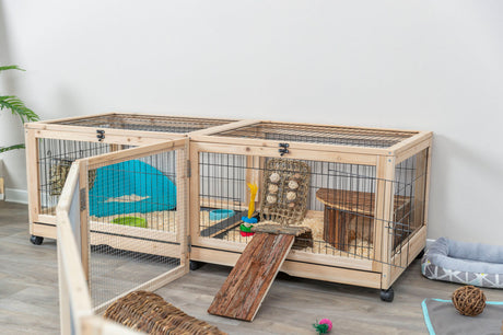 Holzkäfig mit Drahtgitter und Rampen, ausgestattet mit Spielsachen und Liegeflächen, steht auf einem Holzboden.