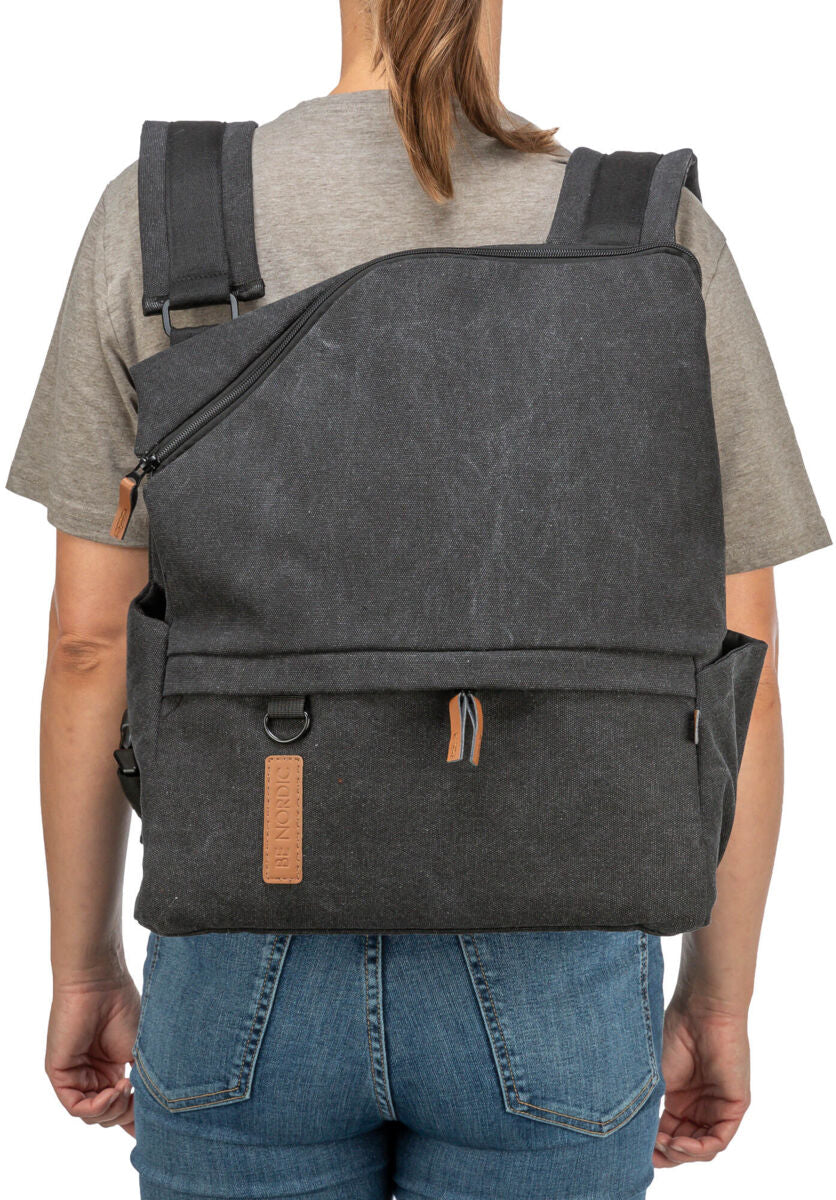 Person von hinten mit grauem Rucksack, trägt graues T-Shirt und blaue Jeans, Rucksack mit Taschen und Lederetikett.