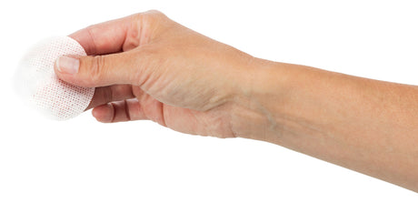 Eine Hand hält ein rundes weißes, perforiertes Pad oder Tuch vor weißem Hintergrund, das zwischen Daumen und Zeigefinger fixiert ist.